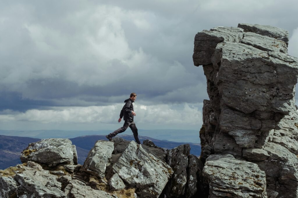 A solitary hiker navigating rocky terrain against a dramatic Scottish sky.